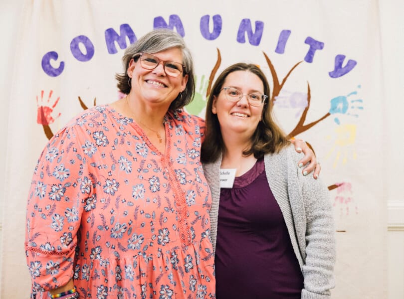 Two women standing in front of a banner that says &quot;Community&quot;