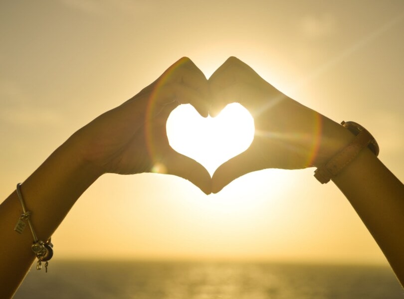 Sunlight pouring through hands in the shape of a heart