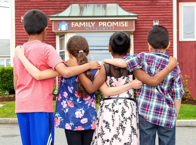 Four children with arms over each others shoulders looking at the Family Promise shelter.