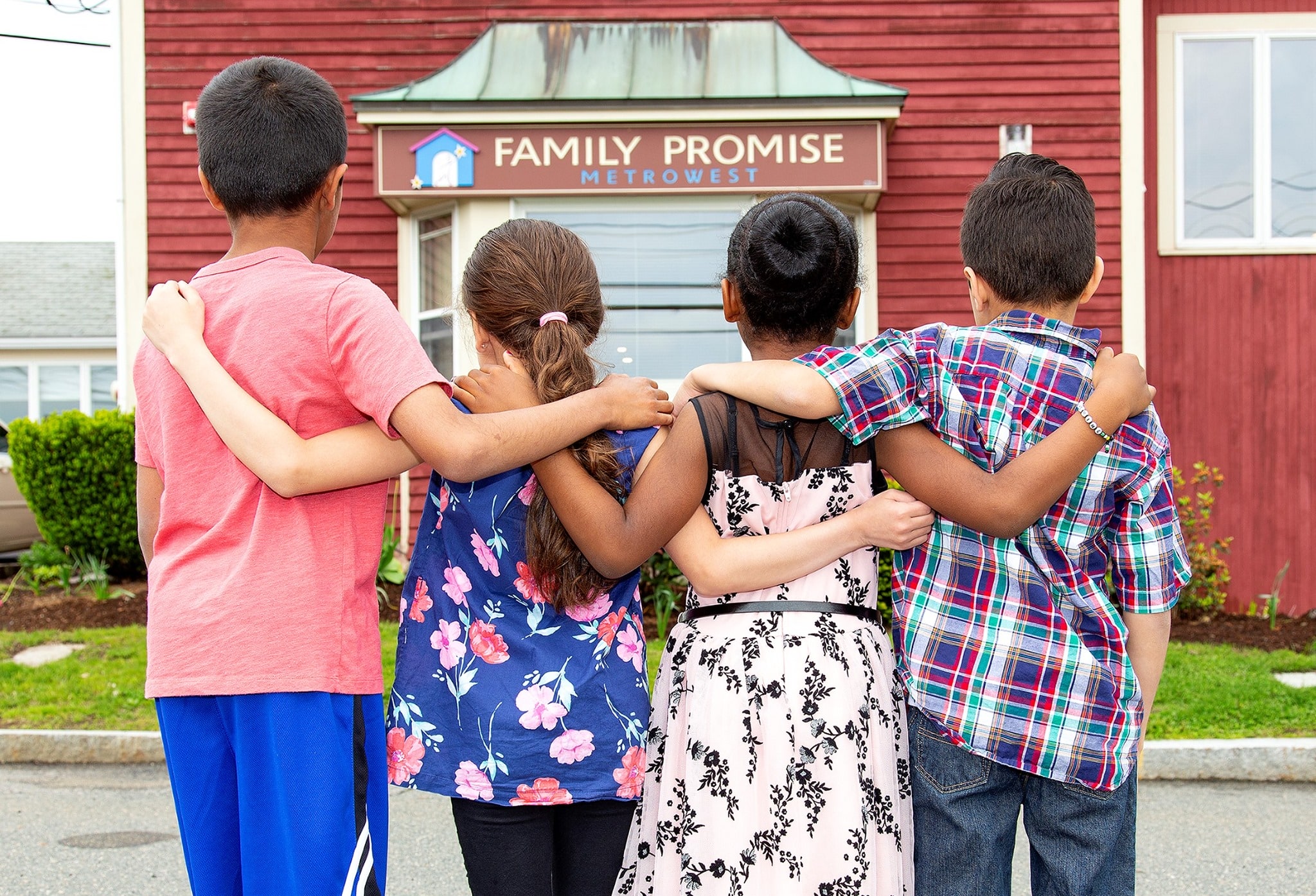 fpmw Four children with arms over each others shoulders looking at the Family Promise shelter.