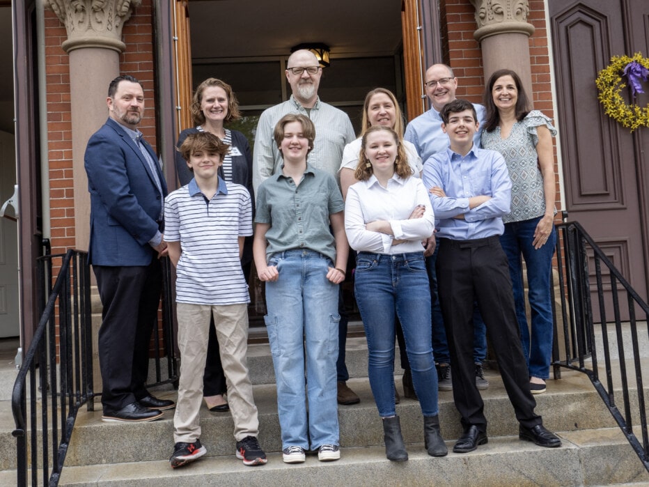 Four thirteen year olds and their parents posing on the front steps of a church.