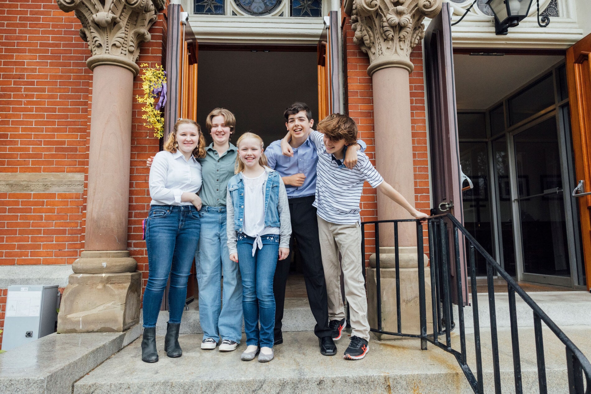 A group of teens stand in front of the church with their arms around one another