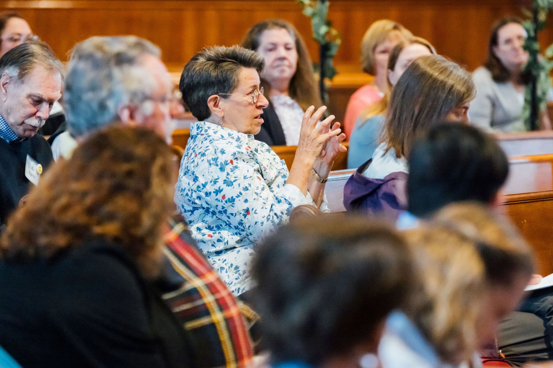A woman in a crowd of adults speaks and gestures with her hands