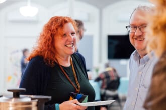 A woman holds a plate and smiles while a man looks on