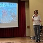 Woman speaking on stage with slide presentation.