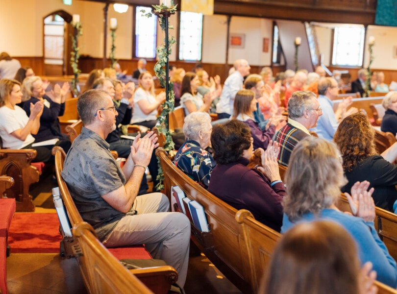 Dozens of people clapping from church pews.