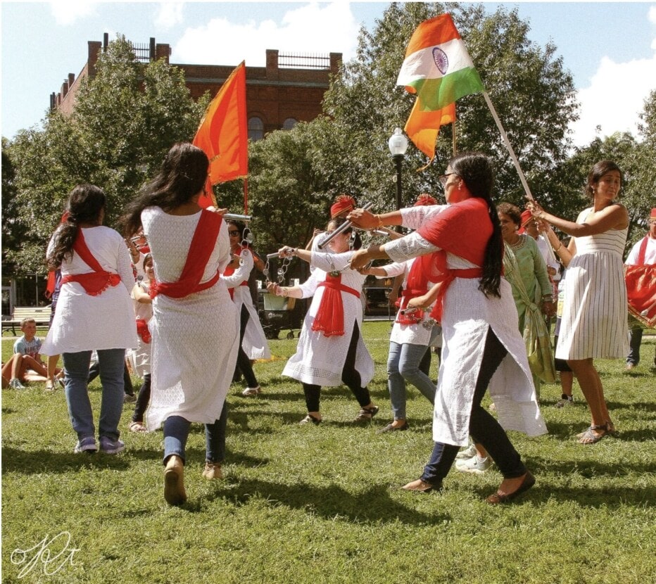 Women in white robes with red sashes engage in a traditional dance