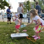 Children blow giant soap bubbles on church lawn.