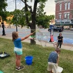 Girl makes a giant soap bubble as parent watches.
