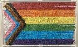 Rainbow flag art made from strips of cloth, each with a handwritten statement.