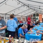 Several tables of people sit down to eat at the church barbeque.