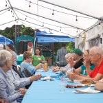 Several tables of people sit down to eat at the church barbeque.