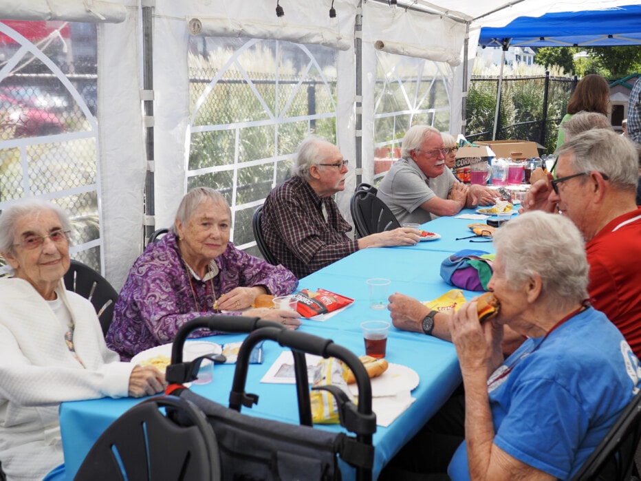 Several tables of people sit down to eat at the church barbeque.