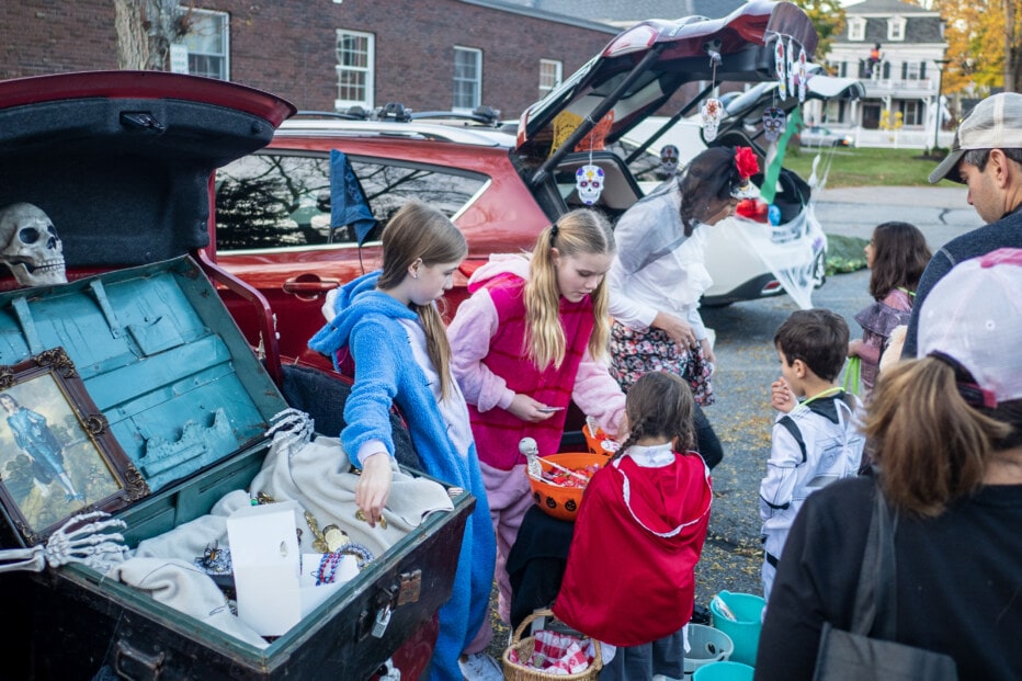 Two youth in costume giving out halloween treats from decorated car trunks.