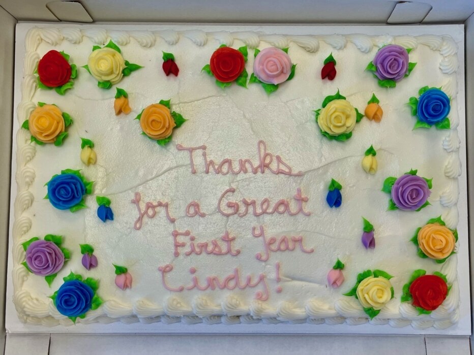 Top view of a cake with colorful icing flowers and the works "Thank you for a great first year Cindy!"