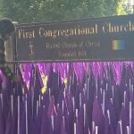 Purple flags on church lawn near church sign.