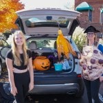 Costumed daughter and mother prepare to give out halloween treats from the back of their car