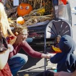 Smiling woman crouches to give halloween candy to small child.