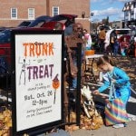 Girl petting a dog skeleton next to Trunk or Treat sign