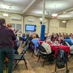 church vestry with people sitting at tables while annual meeting presentation takes place